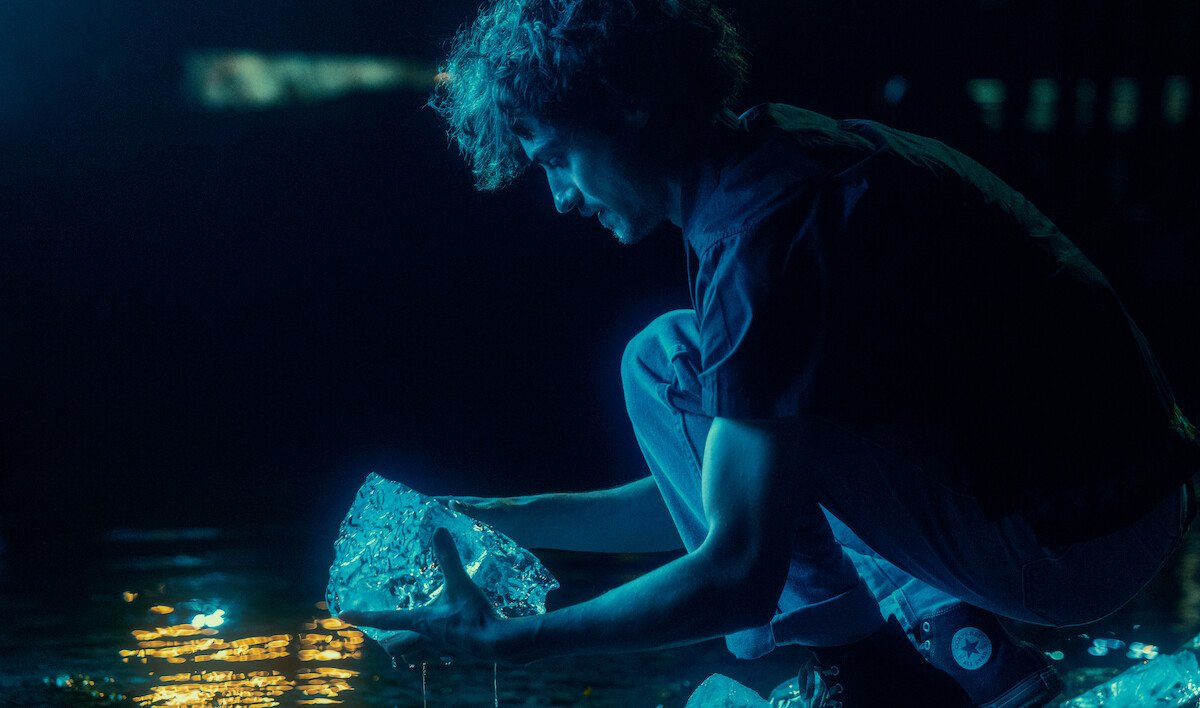 Below ending explained: Wade holds a piece of glowing ice at the water's edge at night